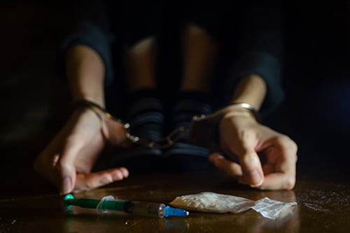 handcuffed woman with syringe and drugs