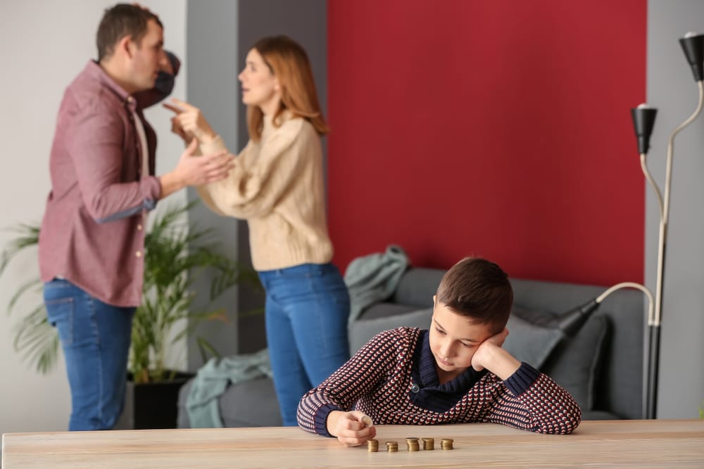 Sad little boy with coins and his quarreling parents at home